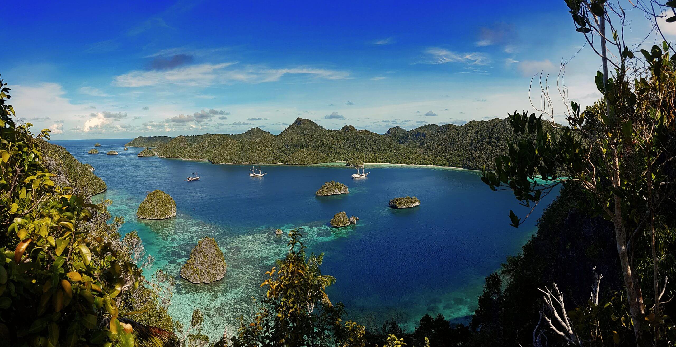 Stunning view of Misool Island, Indonesia, with Karst islets in turquoise water, lush forest, and boats dotting the peaceful lagoon. 