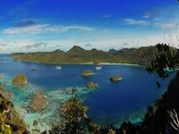 Stunning view of Misool Island, Indonesia, with Karst islets in turquoise water, lush forest, and boats dotting the peaceful lagoon. 