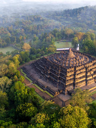 An aerial view of Borobudur Temple surrounded by misty forest in Central Java, Indonesia at sunrise. 