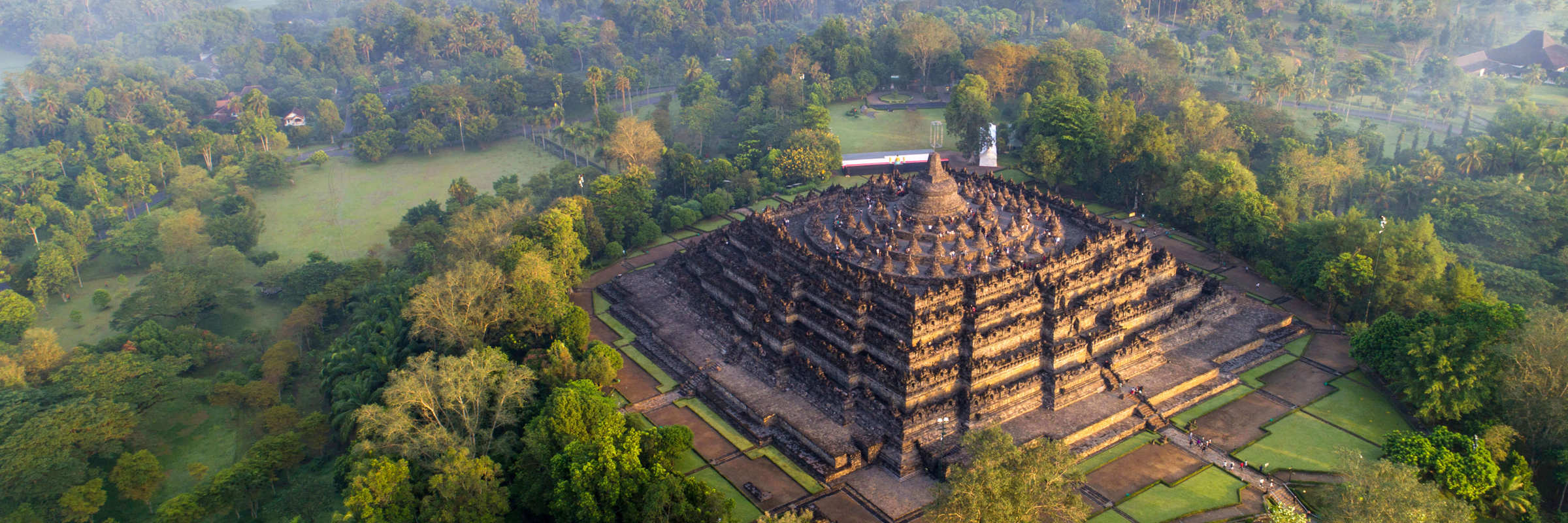 An aerial view of Borobudur Temple surrounded by misty forest in Central Java, Indonesia at sunrise. 