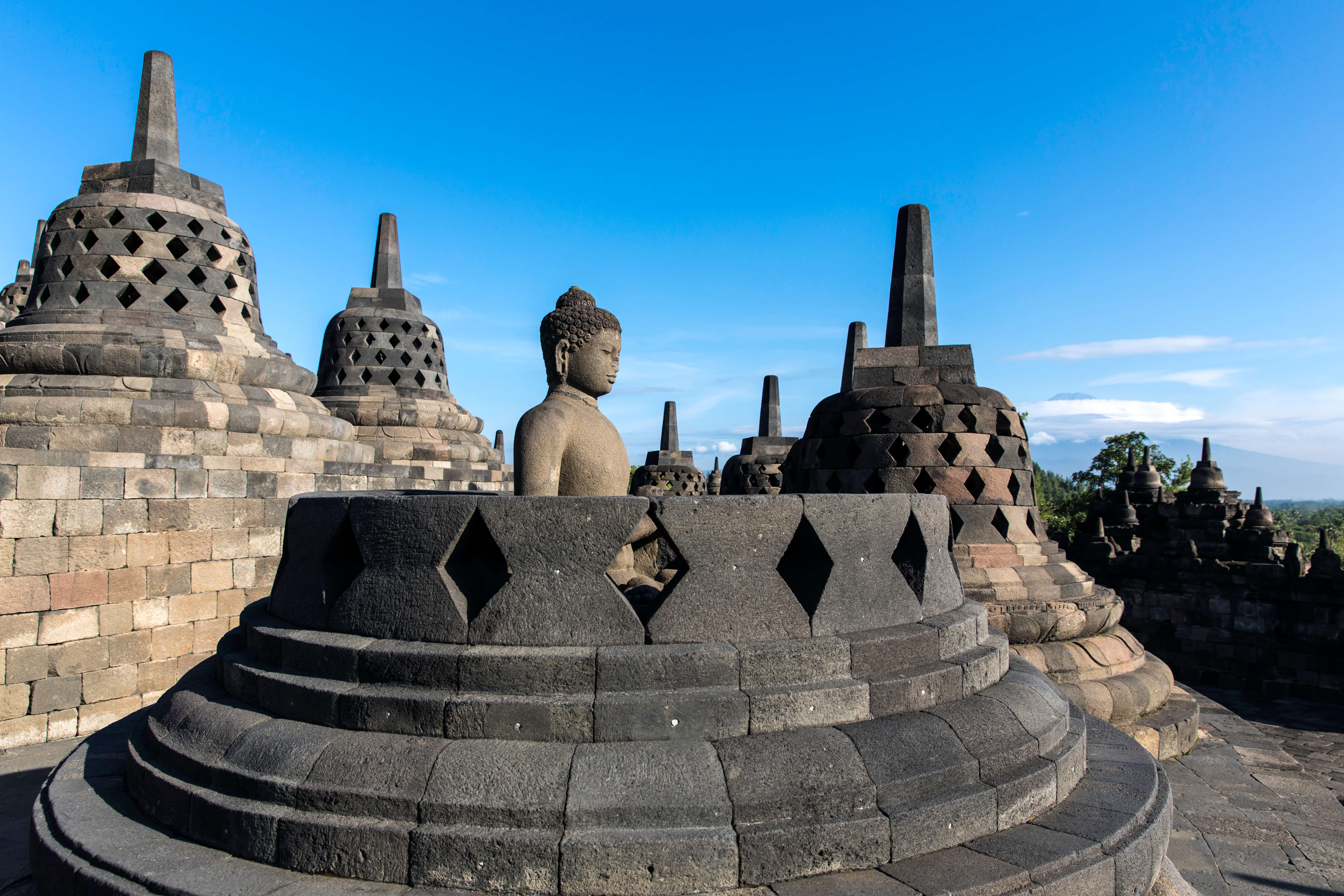 A Buddha statue sits in quiet stillness among stupas at Borobudur Temple in Central Java, Indonesia. 