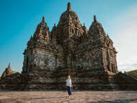 A visitor walks near Sewu Temple, part of the Prambanan complex in Central Java, Indonesia, under a clear blue sky. 