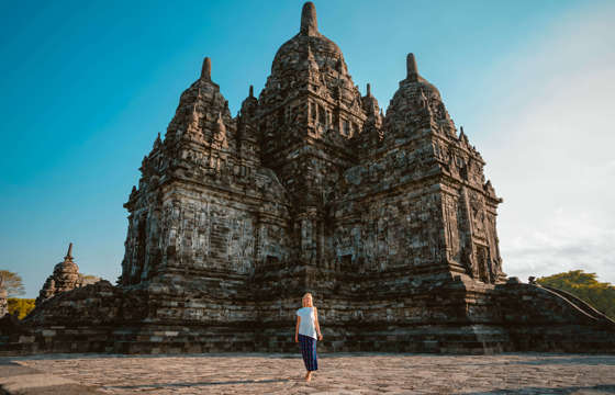 A visitor walks near Sewu Temple, part of the Prambanan complex in Central Java, Indonesia, under a clear blue sky. 