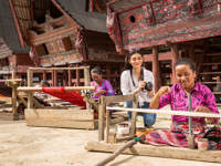 Women weaving textiles in front of  traditional Batak houses near Lake Toba, North Sumatra, Indonesia. 