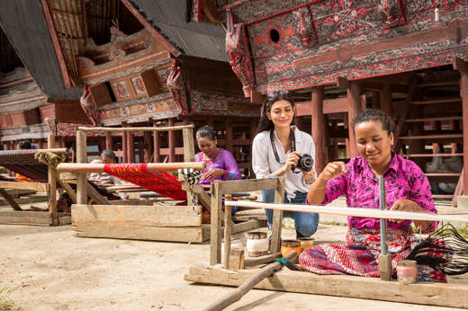 Women weaving textiles in front of  traditional Batak houses near Lake Toba, North Sumatra, Indonesia. 