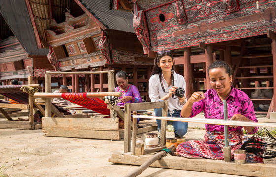 Women weaving textiles in front of  traditional Batak houses near Lake Toba, North Sumatra, Indonesia. 