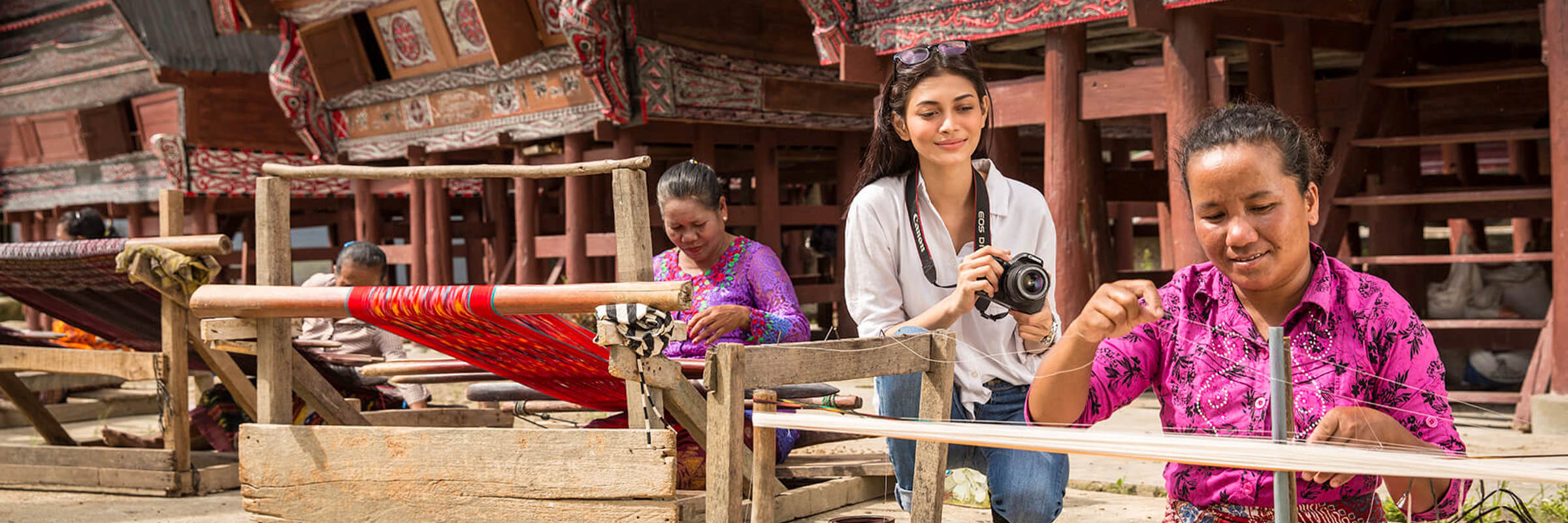 Women weaving textiles in front of  traditional Batak houses near Lake Toba, North Sumatra, Indonesia. 