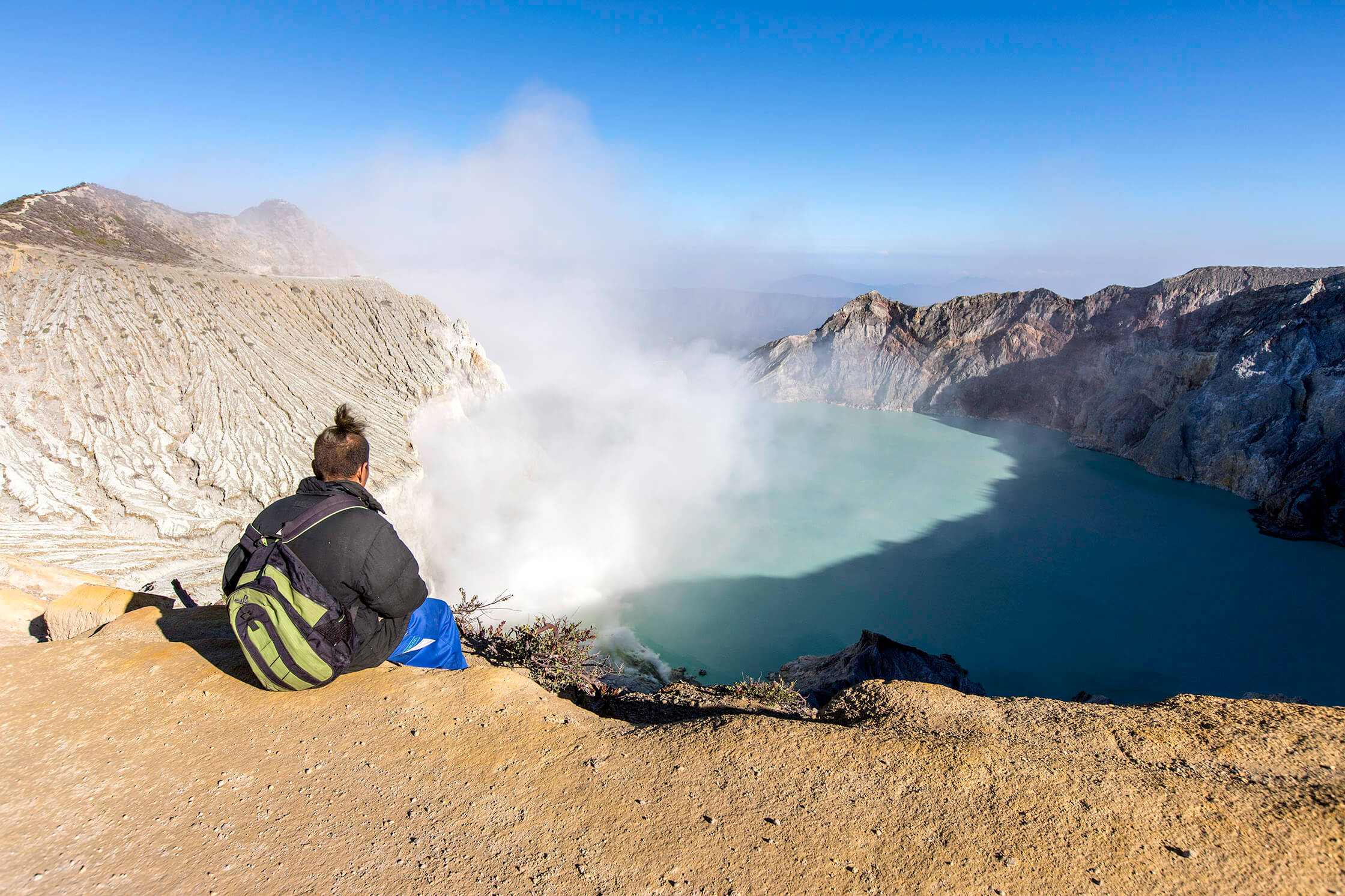 A traveler gazes over the steaming turquoise crater lake of Kawah ljen volcano in East Java, Indonesia. 