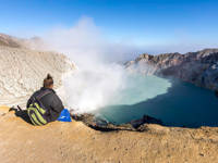 A traveler gazes over the steaming turquoise crater lake of Kawah ljen volcano in East Java, Indonesia. 
