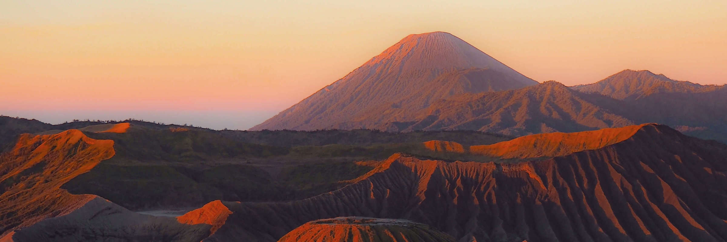 Mount Bromo and surrounding caldera at sunrise in East Java, Indonesia, with soft morning light and volcanic landscape. 