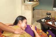 Indonesian woman enjoying a traditional massage at a luxury hotel spa, surrounded by soothing decor and herbal wellness tools. 