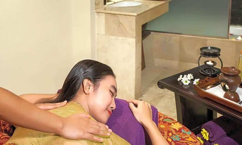 Indonesian woman enjoying a traditional massage at a luxury hotel spa, surrounded by soothing decor and herbal wellness tools. 