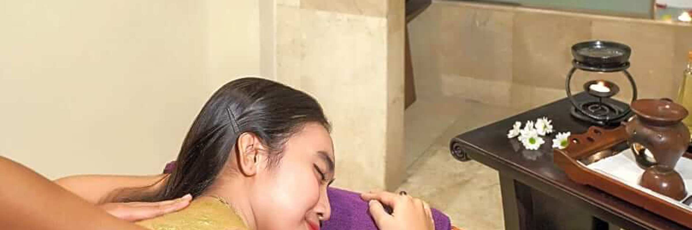 Indonesian woman enjoying a traditional massage at a luxury hotel spa, surrounded by soothing decor and herbal wellness tools. 