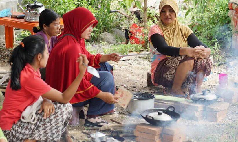 Local women in Bukit Lawang prepare a traditional Indonesian meal over an open fire, showcasing authentic village fire. 