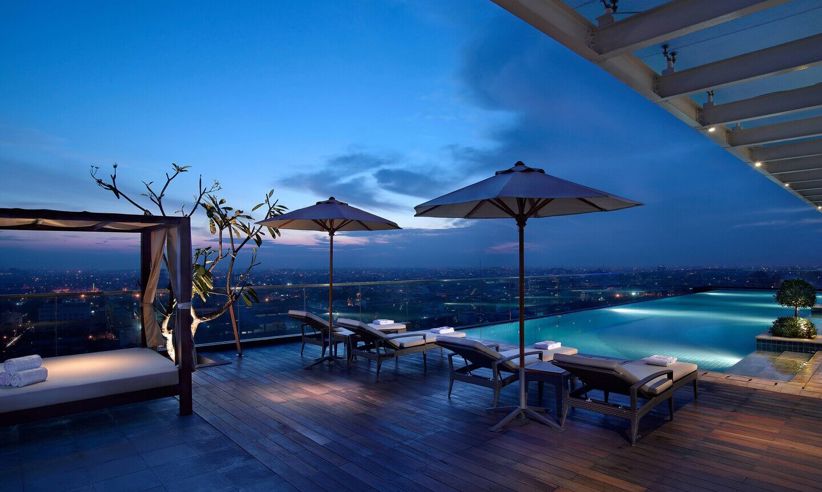 Infinity pool at Marriott Hotel Medan with city lights in the distance, captured during evening twilight. 