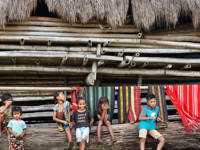 Local children sit by a bamboo hut in a traditional village in Flores, surrounded by colourful handwoven textiles hanging behind them. 