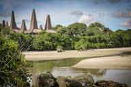 Traditional conical-roof houses of Ratenggaro village in Sumba, Indonesia, seen across a quiet inlet with lush tropical trees. 