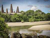 Traditional conical-roof houses of Ratenggaro village in Sumba, Indonesia, seen across a quiet inlet with lush tropical trees. 