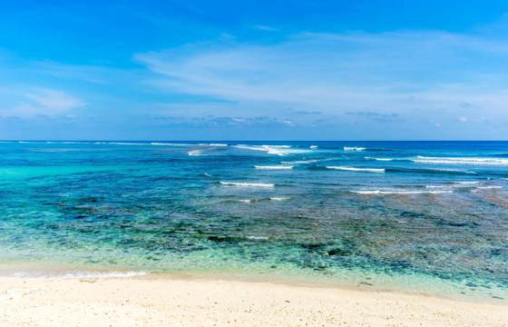 Clear turquoise sea and white sand beach under a bright blue sky on the Gili Islands, Indonesia. 