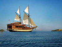 Traditional Indonesian phinisi sailing yacht cruising on calm blue waters on open sails under a clear sky. 