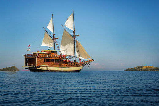 Traditional Indonesian phinisi sailing yacht cruising on calm blue waters on open sails under a clear sky. 