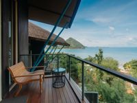 Private balcony suite in Flores, Indonesia with wooden seating, ocean views, and tropical greenery under clear blue skies. 