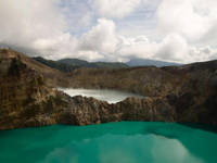 Turquoise crater lake at Kelimutu volcano in Flores, Indonesia, surrounded by rugged cliffs under a cloud sky. 