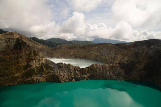 Turquoise crater lake at Kelimutu volcano in Flores, Indonesia, surrounded by rugged cliffs under a cloud sky. 