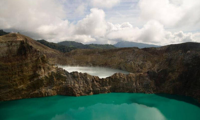 Turquoise crater lake at Kelimutu volcano in Flores, Indonesia, surrounded by rugged cliffs under a cloud sky. 