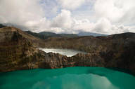 Turquoise crater lake at Kelimutu volcano in Flores, Indonesia, surrounded by rugged cliffs under a cloud sky.