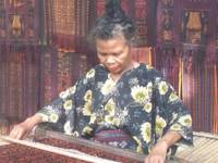 Indonesian woman weaving traditional textiles by hand in Flores, surrounded by rich patterned fabrics in a cultural setting. 