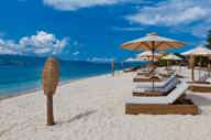 Beachfront sunbeds with umbrellas on the white sands of Gili Trawangan, Lombok, facing turquoise ocean under blue sky. 