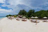 Luxury beach resort on Gili Trawangan with white sand, sun loungers, thatched umbrellas, and lush tropical trees lining the shore. 
