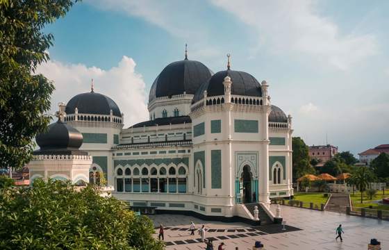 The majestic Grand Mosque of Medan in Indonesia, with its striking domes and intricate architecture, under a clear blue sky. 