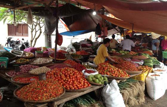 A vibrant traditional market in Amurang, Indonesia, displaying colourful piles of chilies, tomatoes, and fresh produce under shaded stalls. 