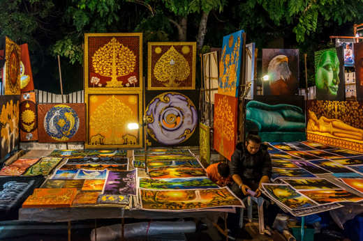 Local Indonesian art market at night with vibrant paintings on display, showcasing traditional and modern cultural designs. 
