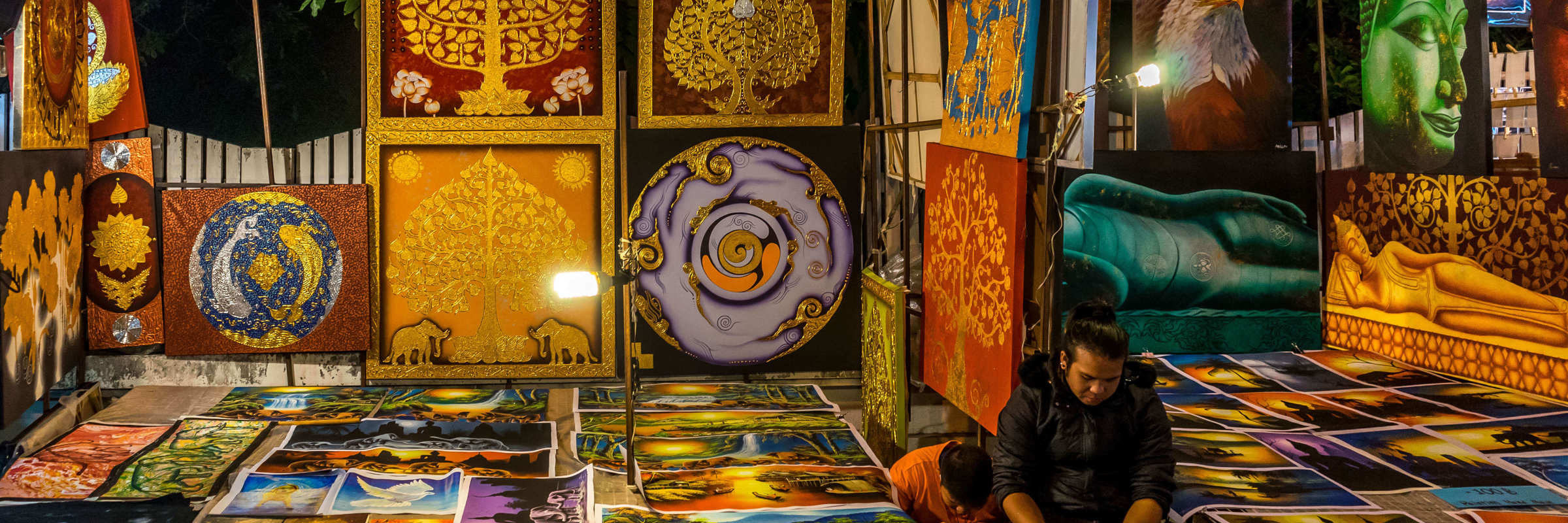 Local Indonesian art market at night with vibrant paintings on display, showcasing traditional and modern cultural designs. 