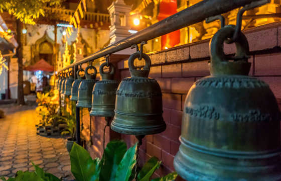 Bronze temple bells hang along a shrine walkway, warmly lit at dusk in a sacred temple complex in Indonesia. 