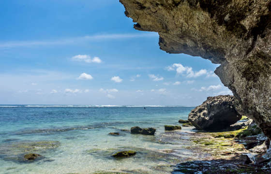 A secluded rocky beach with turquoise water and cliff overhang along Indonesia's stunning tropical coastline. 