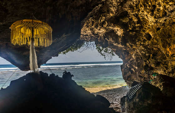 A traditional Balinese shrine stands in seaside cave, facing the ocean at a sacred coastal temple in Bali, Indonesia.