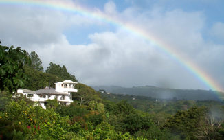 Rainbow arcs over the lush hills and white villa of Finca Rosa Blanca in Costa Rica. 