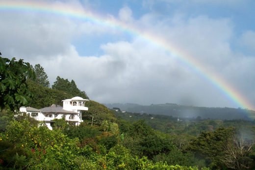 Rainbow arcs over the lush hills and white villa of Finca Rosa Blanca in Costa Rica. 