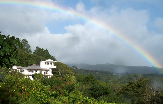 Rainbow arcs over the lush hills and white villa of Finca Rosa Blanca in Costa Rica. 