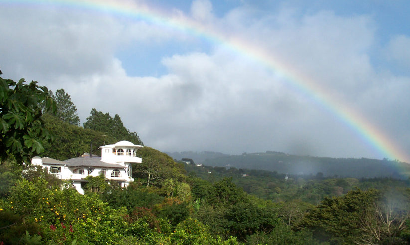 Rainbow arcs over the lush hills and white villa of Finca Rosa Blanca in Costa Rica. 