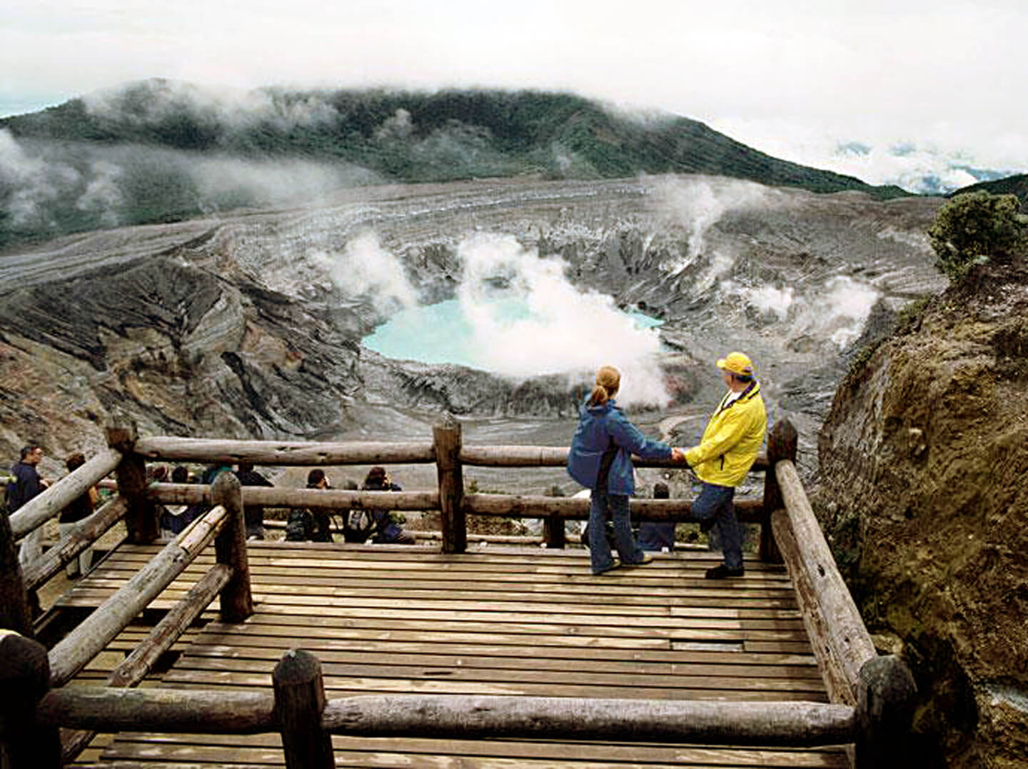 A couple enjoying the dramatic view of Poas Volcano's steaming crater from a wooden observation platform in Costa Rica. 
