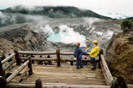 A couple enjoying the dramatic view of Poas Volcano's steaming crater from a wooden observation platform in Costa Rica. 