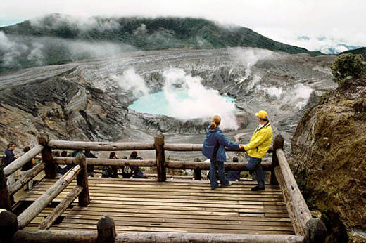 A couple enjoying the dramatic view of Poas Volcano's steaming crater from a wooden observation platform in Costa Rica. 