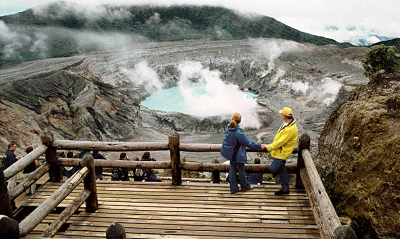 A couple enjoying the dramatic view of Poas Volcano's steaming crater from a wooden observation platform in Costa Rica. 