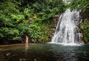 A tourist enjoys a refreshing dip beneath a cascading waterfall in the lush Rincon de la Vieja rainforest. 