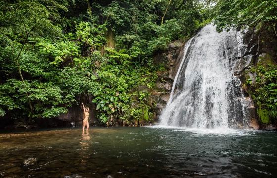 A tourist enjoys a refreshing dip beneath a cascading waterfall in the lush Rincon de la Vieja rainforest. 